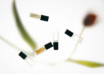 Several small glass perfume bottles with black caps scattered among blurred floral stems on a bright white background.
