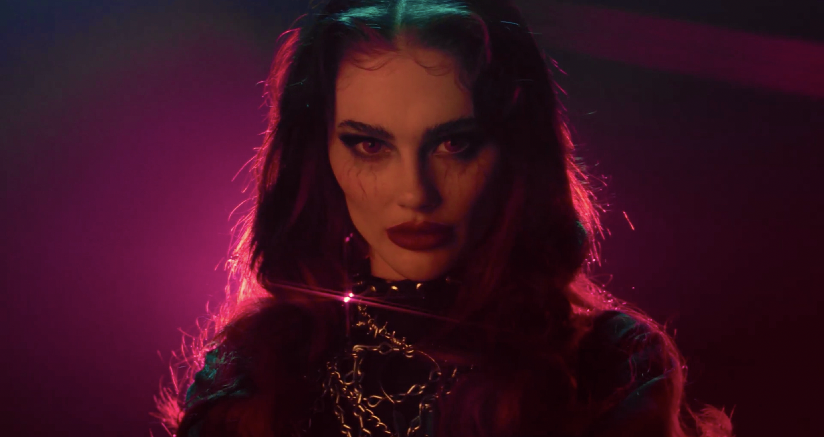 Close-up portrait of a young adult female with long, dark red hair wearing a black choker and heavy chain in a dimly lit studio.