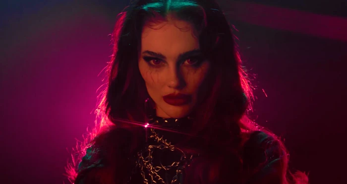 Portrait of a woman with dark hair, bold makeup, and chains, under dramatic red lighting directed by Felice Vale