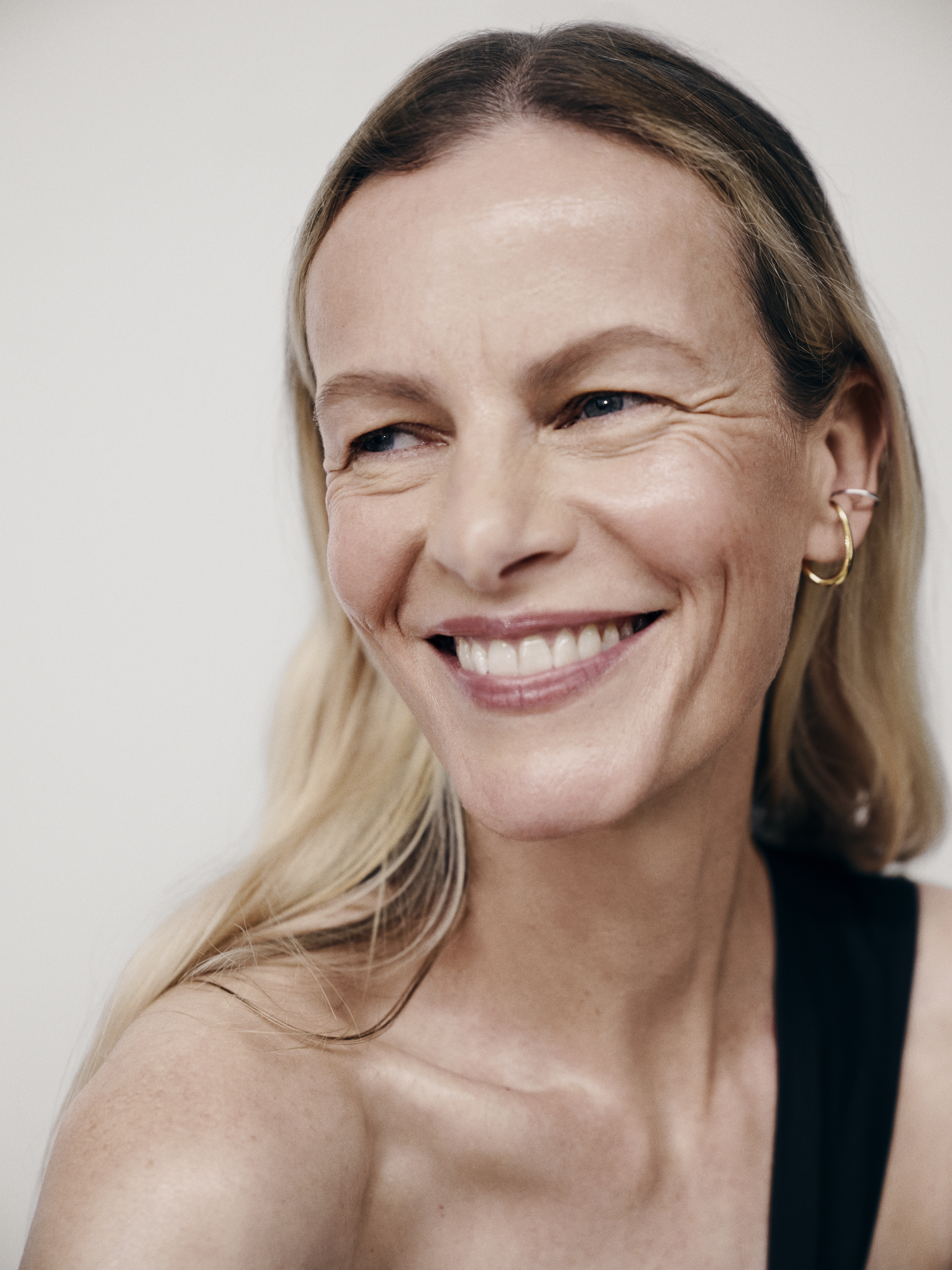 Smiling adult woman with blonde hair and black top against a white background in a close-up shot for beauty and fashion.