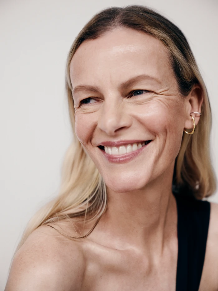 Close-up portrait of a smiling older woman wearing a gold ear cuff against a plain light background