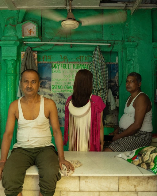 Indoor shot of two adult men and a woman with long hair in front of a green wall with hanging clothes and visible retail signage.