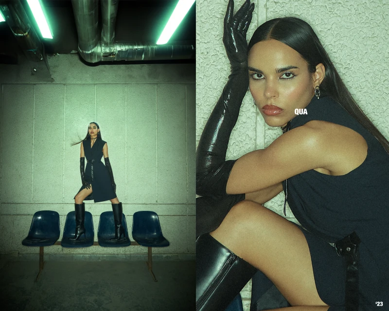 Fashion editorial shot of a woman in a black dress and gloves, posing in an urban environment with chairs and pipes.