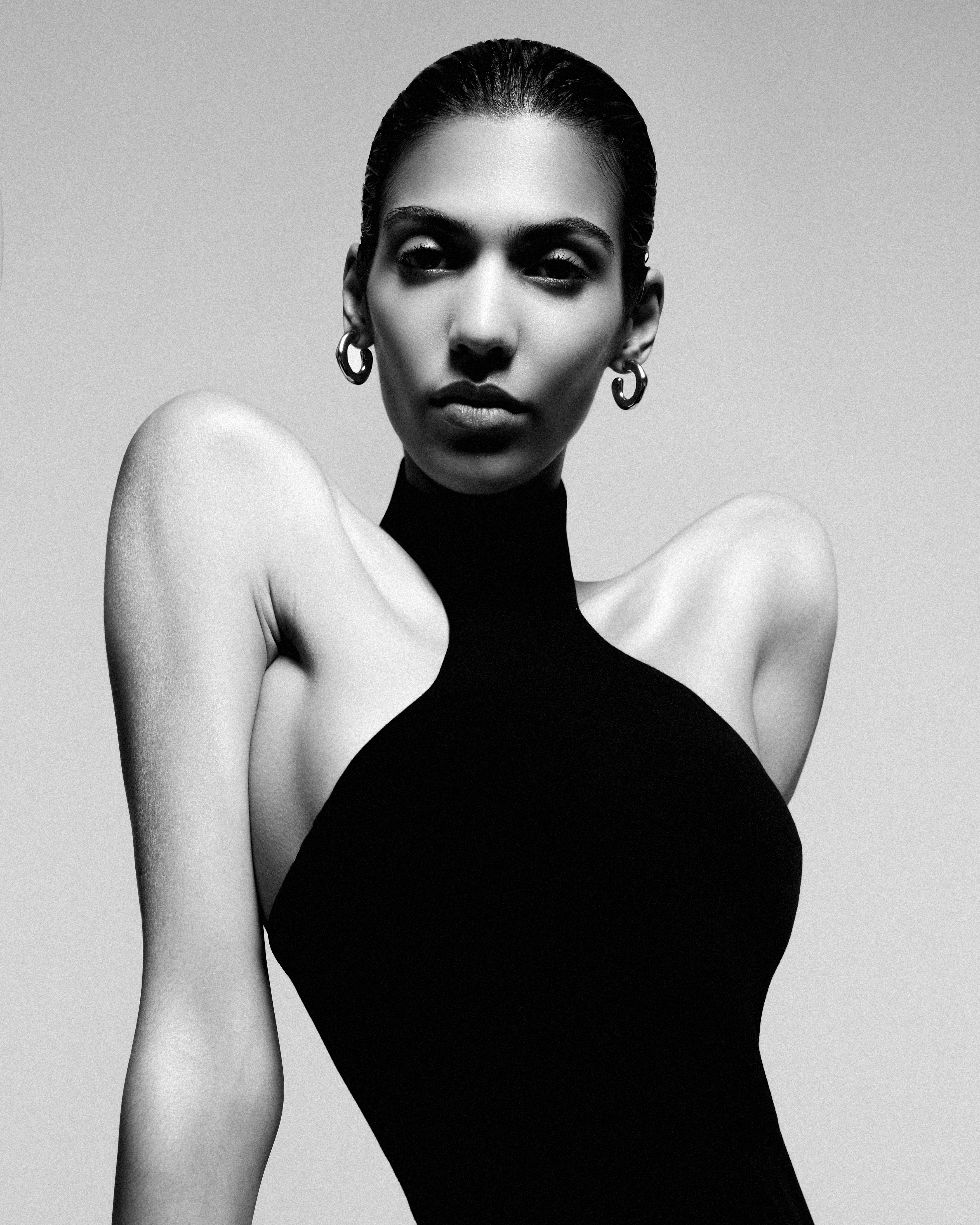 Striking black and white portrait of a woman in a high-neck black top against a neutral backdrop. Focus is on her face and elegant pose.