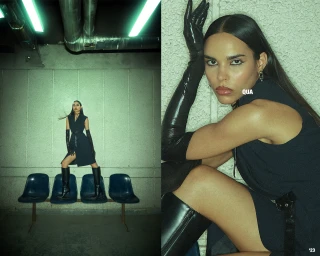 Woman in dark sleeveless dress wearing long black gloves and knee-high boots posing on chairs under a green-lit industrial ceiling.