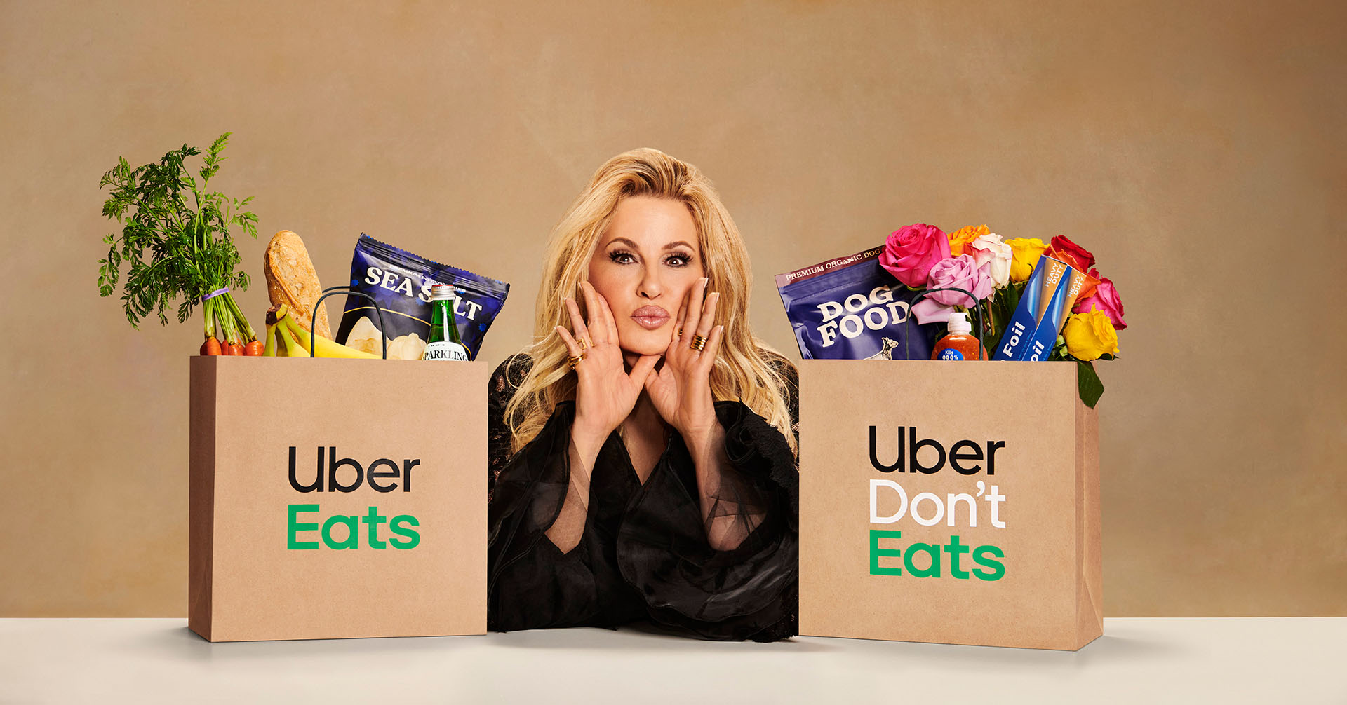Jennifer Coolidge poses between two paper shopping bags, one labeled Uber Eats with food and the other Uber Don't Eats with flowers.