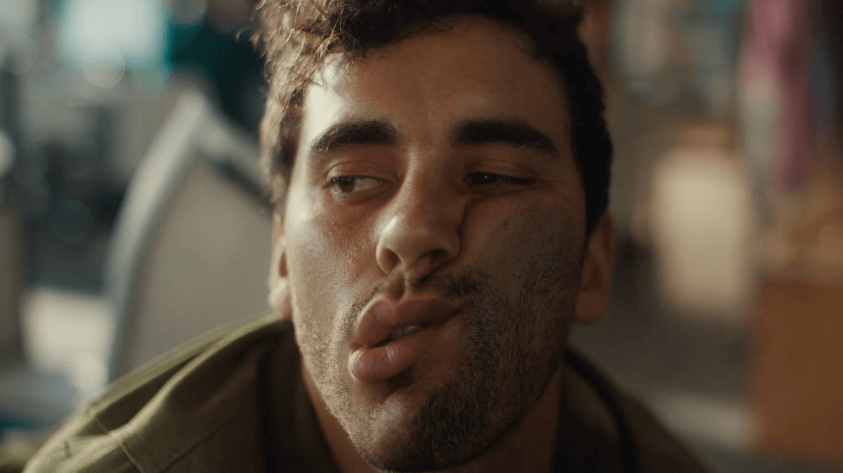 Close-up shot of a young adult male with a slightly dirty face, wearing an olive green jacket, pulling a funny face with his lips puckered.