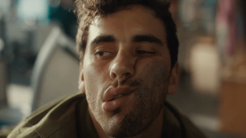 Close-up shot of a young adult male with a slightly dirty face, wearing an olive green jacket, pulling a funny face with his lips puckered.