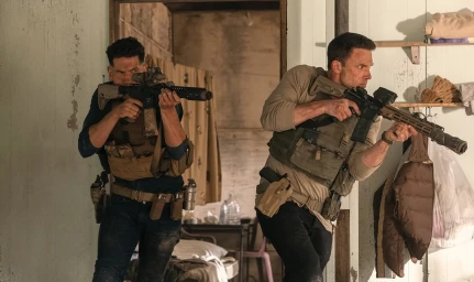 Two men in tactical gear holding assault rifles indoors near a doorway, produced by Artists Equity.