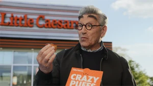 Man holding a Crazy Puff snack from Little Caesars, standing in front of the restaurant on an overcast day in an eye-level shot.