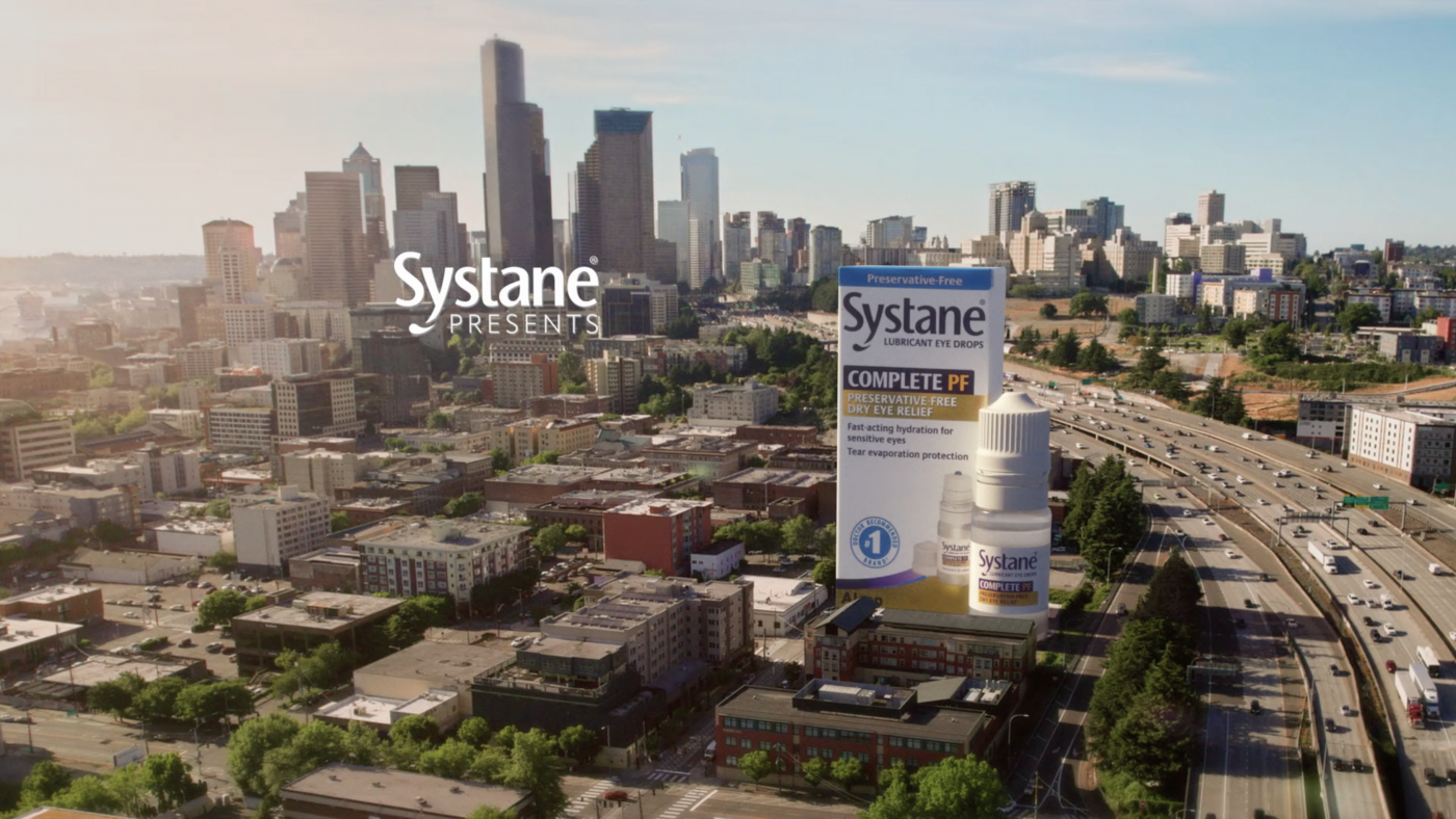 Product shot of Systane Complete PF lubricant eye drops with a cityscape and highway in the background, product and urban focus.