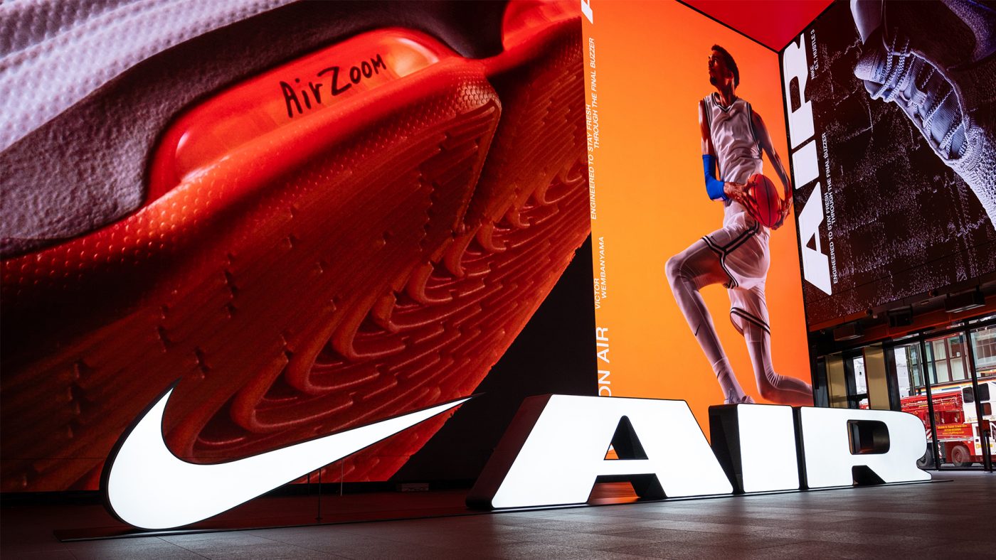 Nike Air Zoom shoe display with basketball player Victor Wembanyama in a basketball uniform jumping, set against an orange backdrop.