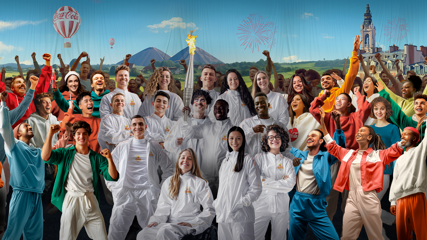 Large group of diverse people smiling with raised arms in front of a light blue sky with buildings and hot air balloons in background.