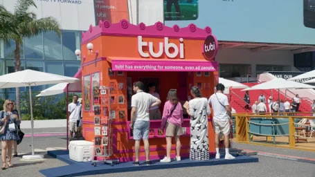 Bright orange and pink Tubi branded promotional newsstand kiosk outdoors in Los Angeles with people gathered around