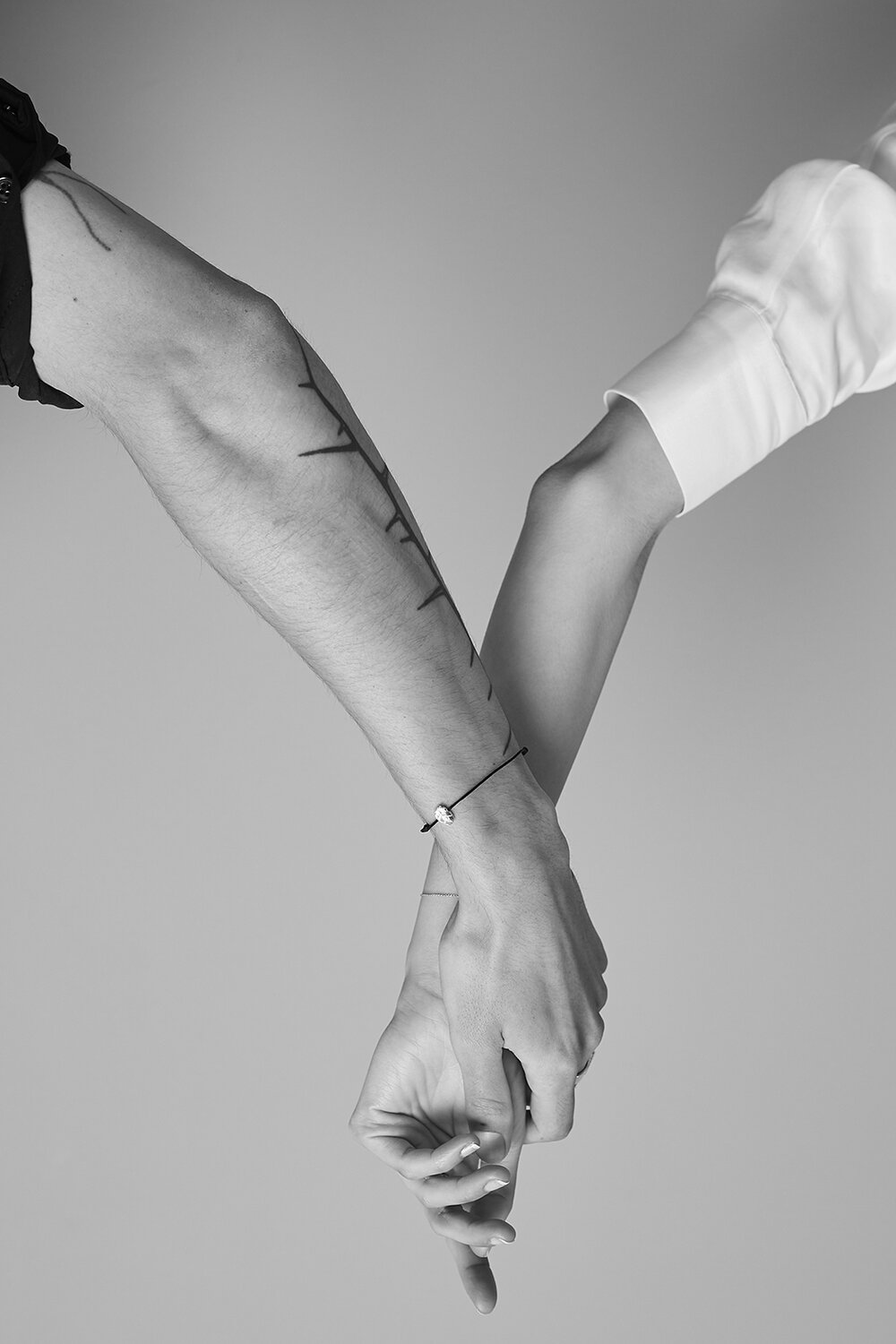 Monochrome image of two people holding hands, with visible forearms, one person wearing a white shirt and the other a black shirt.