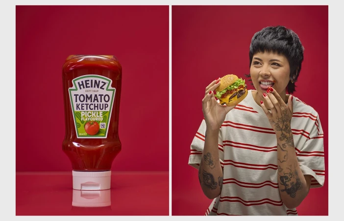 A woman with a burger and a bottle of Heinz pickle-flavored ketchup set against a red background in a food-themed studio shot.