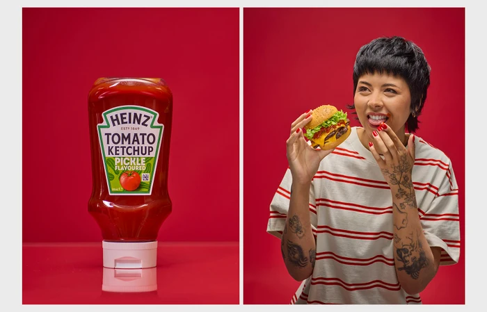 Heinz tomato ketchup bottle next to a woman holding a cheeseburger against a solid red background