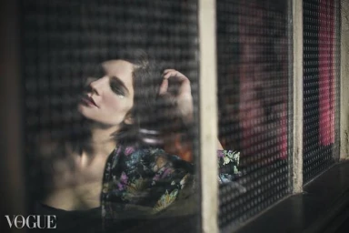 Woman in floral patterned top behind a textured grid window viewed from Melbourne by Catherine Black