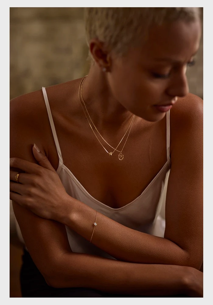 Close-up portrait of a woman with short blonde hair wearing layered gold necklaces and a delicate white camisole.
