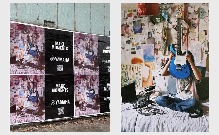 Person holding a blue electric guitar in front of their face, sitting on a bed in a bedroom covered in posters and notes.