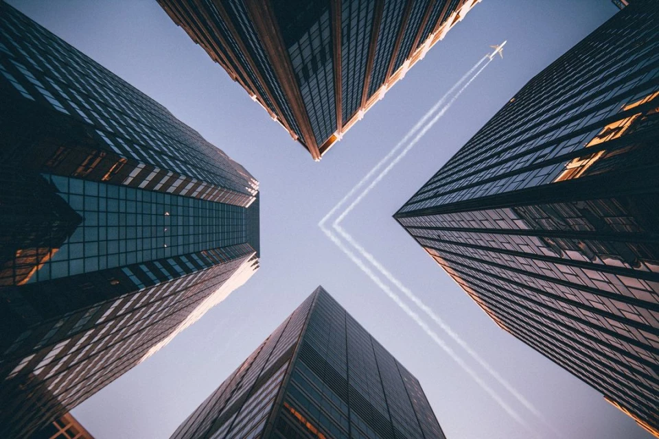 Low angle view of skyscrapers reaching toward the sky with airplane contrails above, creating a modern urban landscape.