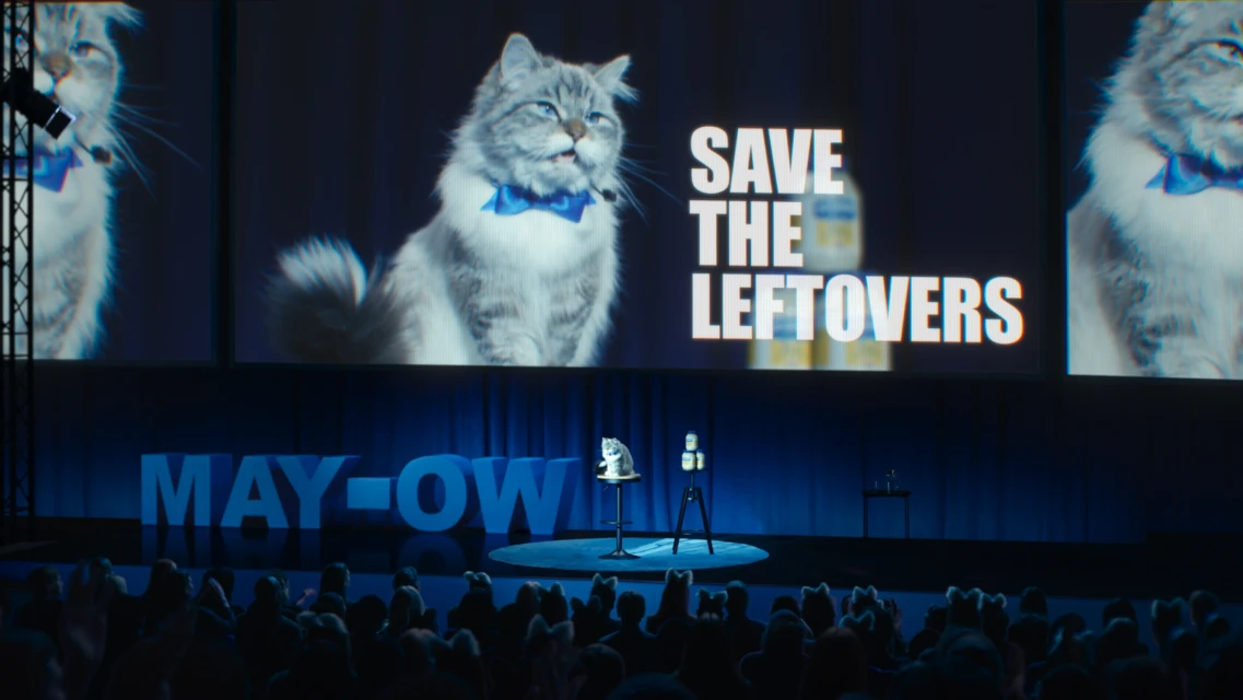 A stage presents a cat 'MAY-OW' event to an audience with cat-ear headbands, emphasizing animal-themed entertainment and a playful setting.
