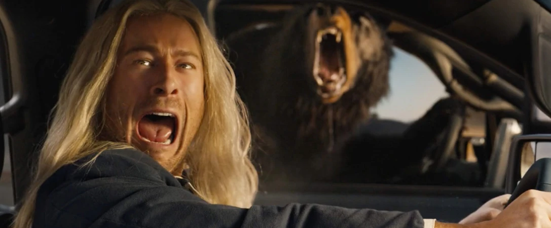 Man in car screams, startled by a roaring bear outside. Scared expression, long hair, vehicle interior, outdoor setting.