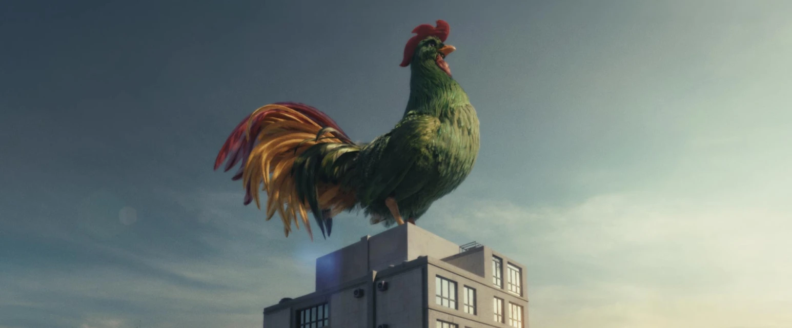 A large green rooster stands atop a gray building under a blue sky, creating a surreal and eye-catching visual composition.