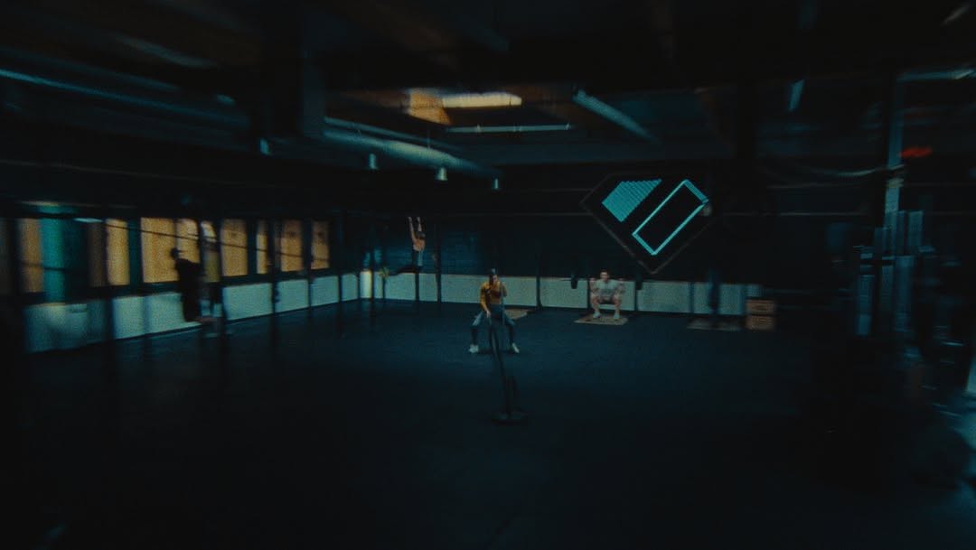 Several athletes engaging in various fitness activities inside a dimly lit gym, performing squats, chin ups, and battle rope exercises.