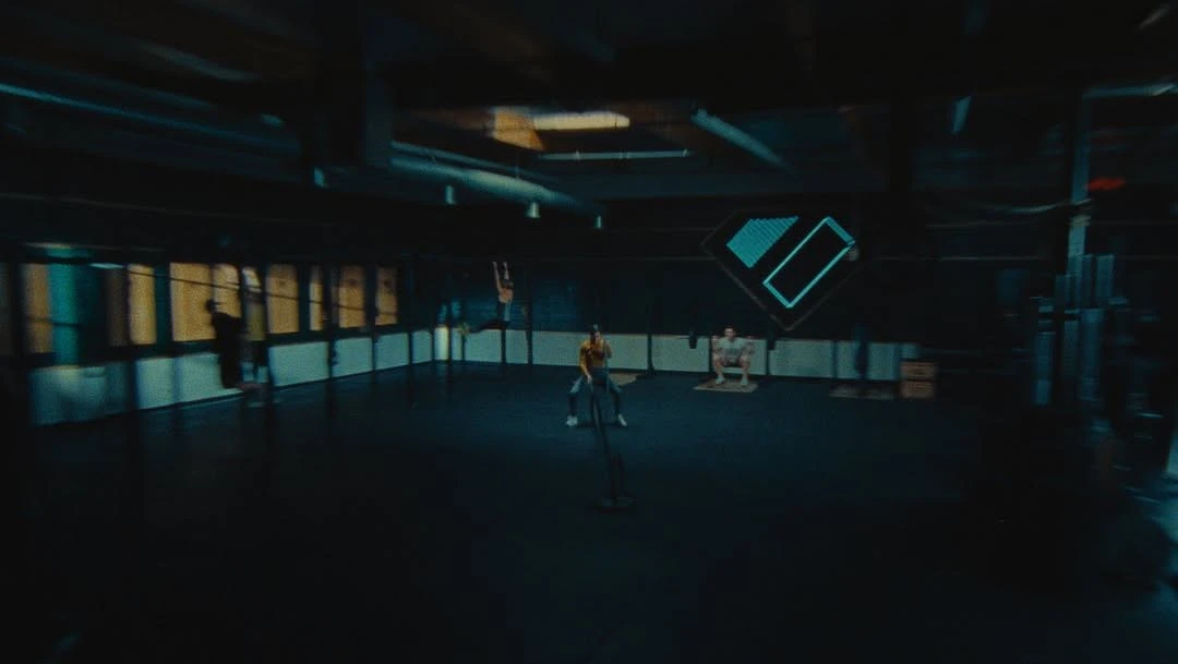 Several athletes engaging in various fitness activities inside a dimly lit gym, performing squats, chin ups, and battle rope exercises.