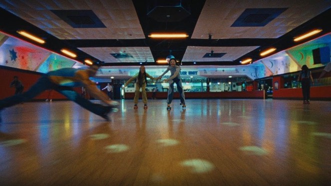 People roller skating in an indoor rink, brightly lit with wood floor. Skaters moving with motion blur and dynamic posing indoors.