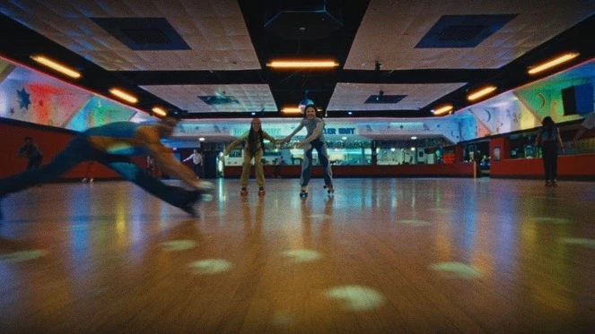 People roller skating in an indoor rink, brightly lit with wood floor. Skaters moving with motion blur and dynamic posing indoors.