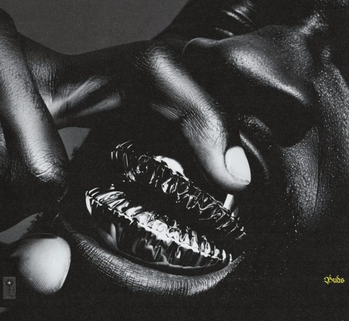 Close-up of adult hands holding metallic lips in a monochrome studio photograph; skin contrasts with a glossy reflective lip prop.