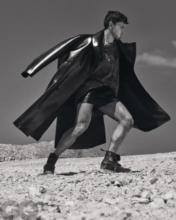Monochrome fashion portrait of a man in a long coat and dark shorts outdoors on rocky terrain