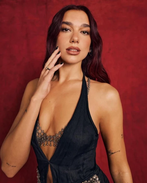 Portrait of a woman with dark hair in a black halter top, standing against a dark red background with dramatic lighting. 