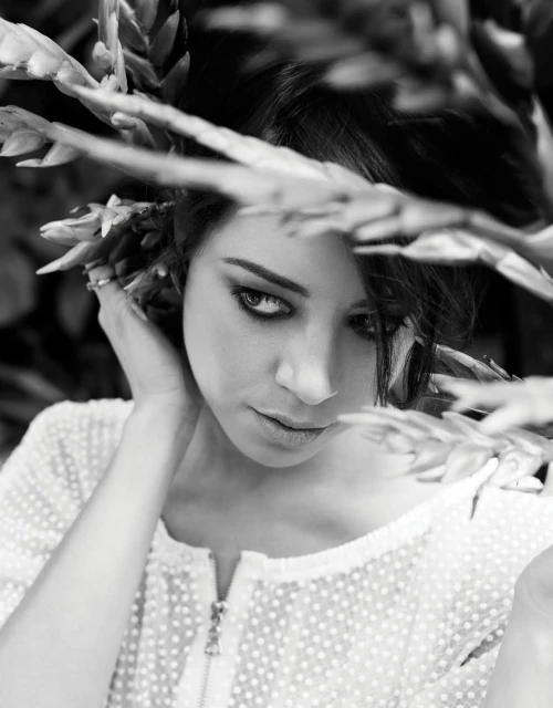 Portrait of a woman in black and white with dark hair, posed among tropical vegetation in an outdoor setting, wearing a textured shirt.