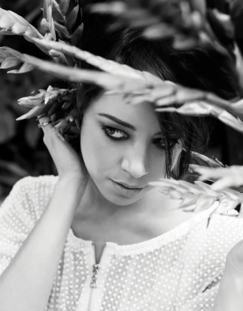 Portrait of a woman in black and white with dark hair, posed among tropical vegetation in an outdoor setting, wearing a textured shirt.
