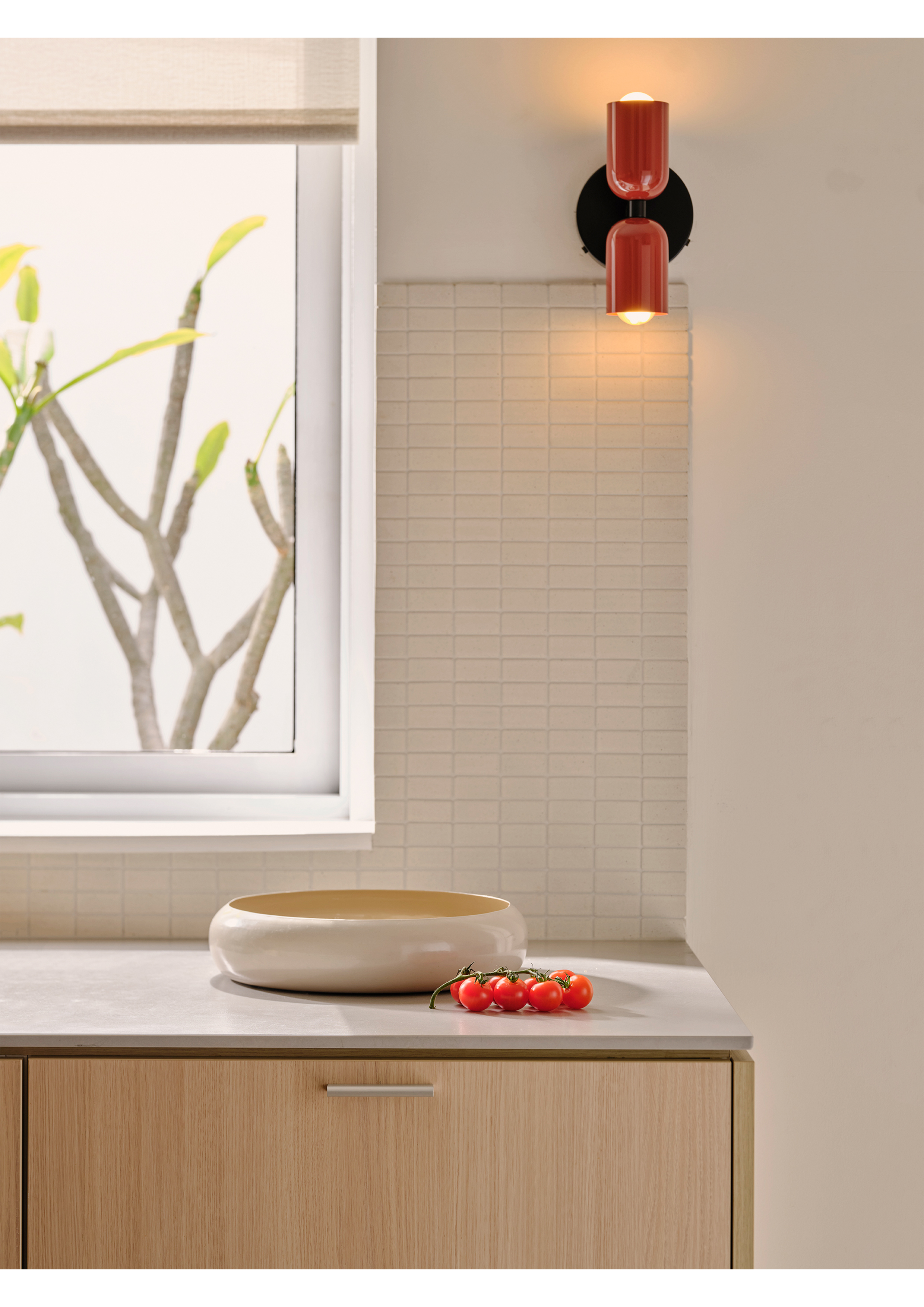 Interior shot of modern kitchen with a ceramic bowl and tomatoes on a marble countertop near a window and a red sconce.