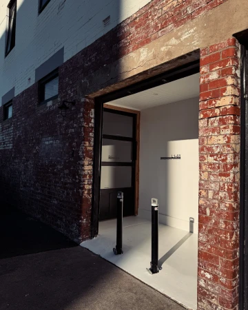 Exterior view of a building's entrance, featuring a brick facade with a doorway leading to a bright, minimalist interior space.