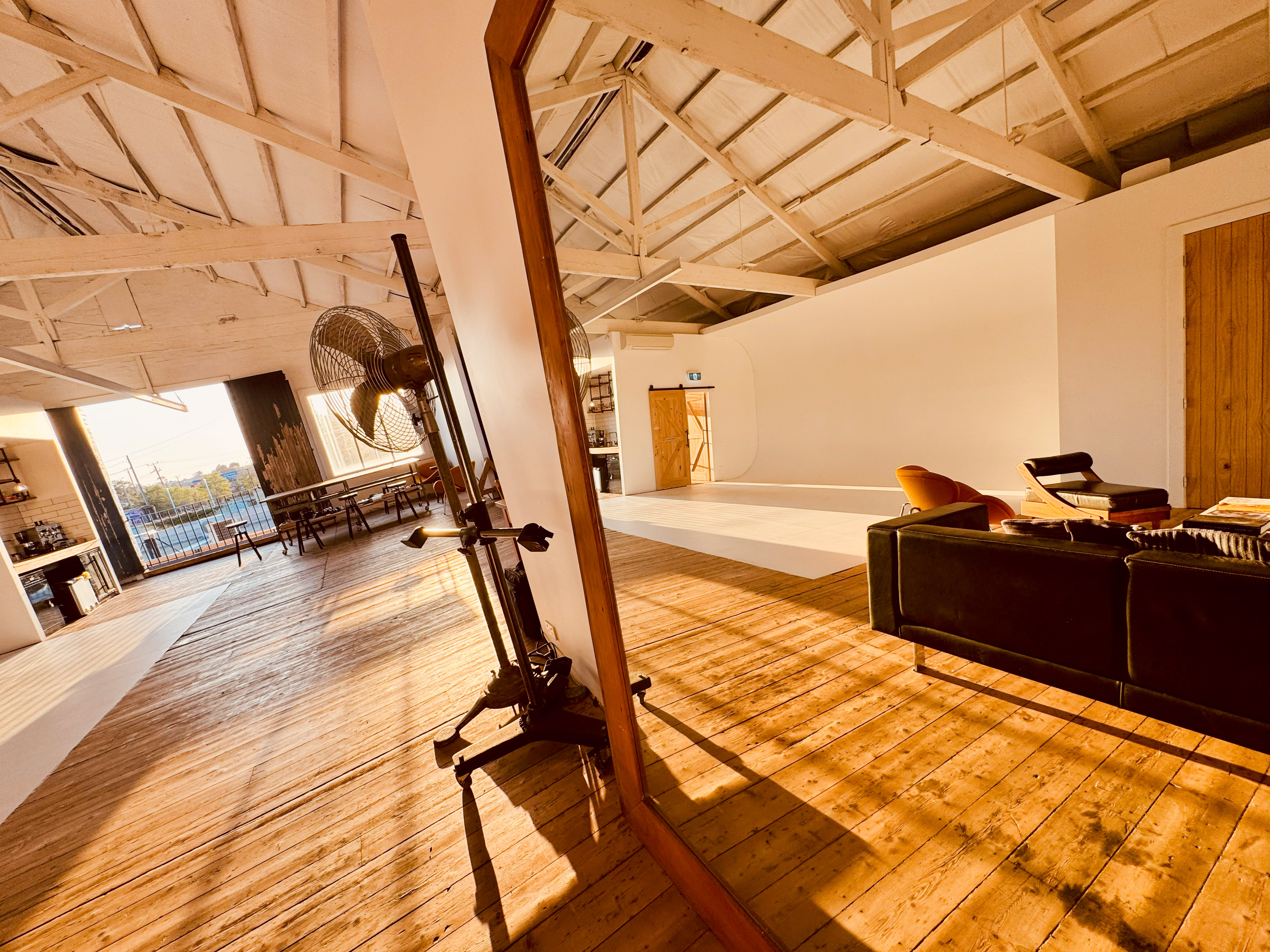 Spacious photo studio interior with natural light, wooden floors, minimal furniture, and photography equipment.
