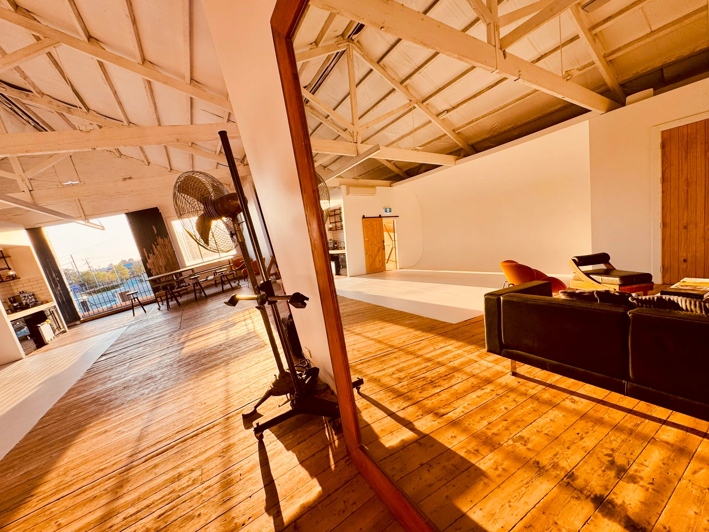 Spacious photo studio interior with warm sunlight casting long shadows across polished wooden floorboards and white walls.