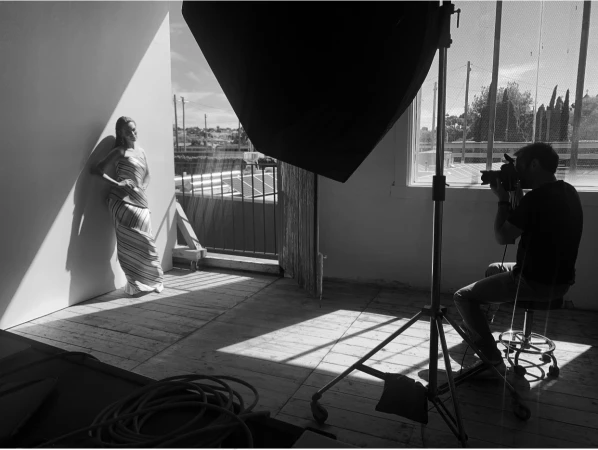 Behind-the-scenes photo of a photographer capturing a model posing in a striped dress inside a studio by Mercer and Roy Studios
