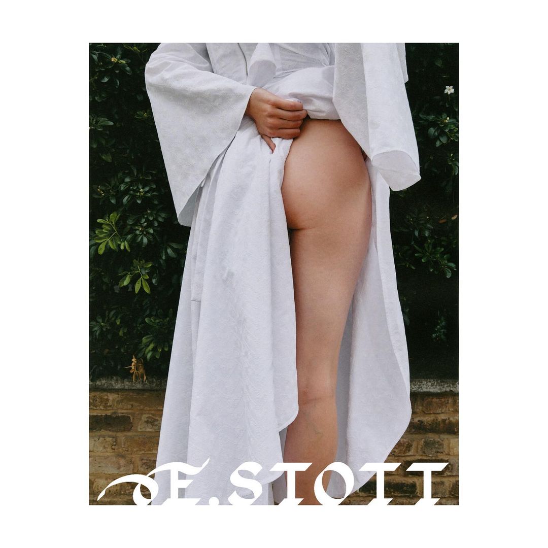 A fair-skinned human is pictured from the lower back to the upper thighs, wearing a white robe and standing in front of a brick wall.