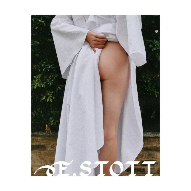 A fair-skinned human is pictured from the lower back to the upper thighs, wearing a white robe and standing in front of a brick wall.