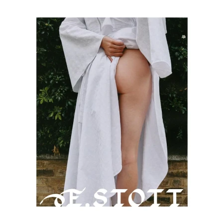A fair-skinned human is pictured from the lower back to the upper thighs, wearing a white robe and standing in front of a brick wall.
