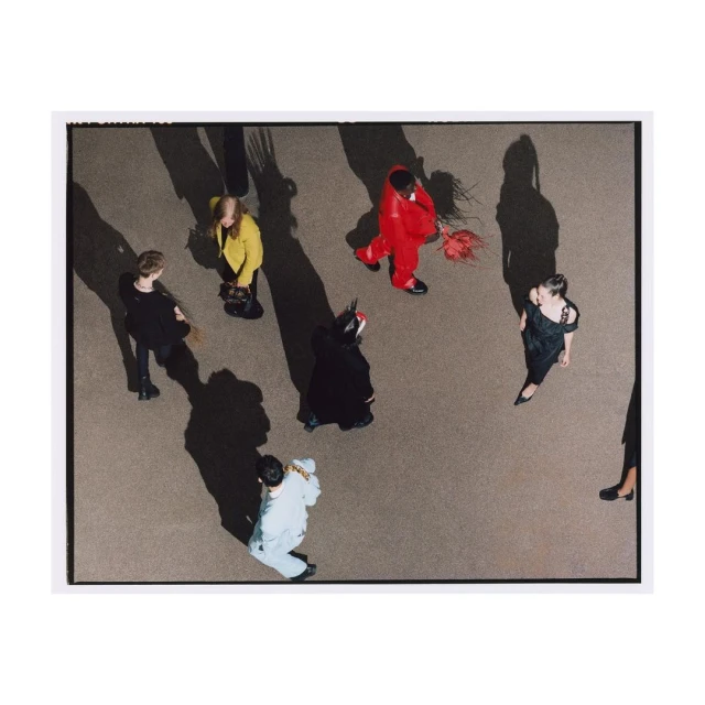 High-angle shot of a group of people dressed in various costumes standing on a brown surface with long shadows, creating a dynamic composition.