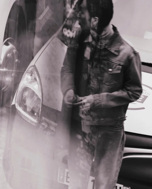 Man in a denim jacket stands near a car, with a superimposed effect creating a blended scene, rendered in black and white.