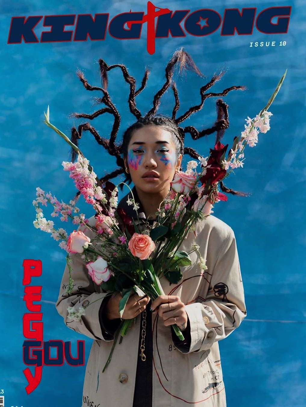 King Kong magazine cover featuring a model with floral hair accessories, a trench coat, and colorful makeup against a blue backdrop.