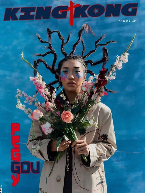 King Kong magazine cover featuring a model with floral hair accessories, a trench coat, and colorful makeup against a blue backdrop.