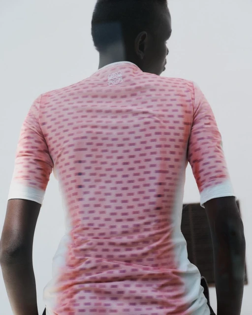 Back view of an adult wearing a pink short-sleeved shirt with a geometric pattern, standing in front of a light neutral wall.